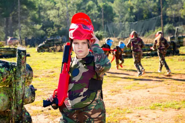 Photo of Boy paintball player in camouflage standing with gun before playing outdoors