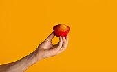 Millennial guy holding yummy fresh muffin over orange background, closeup