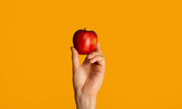 istock Male hand showing yummy red apple on orange background 1271709256