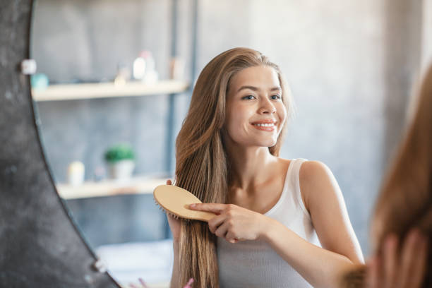 retrato de la dama rubia alegre cepillando su pelo largo cerca de mirar vidrio en el baño - cabello largo fotografías e imágenes de stock