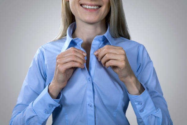 código de vestimenta formal de negocios - sonriente mujer abotonando blusa azul - abrochar su camisa fotografías e imágenes de stock