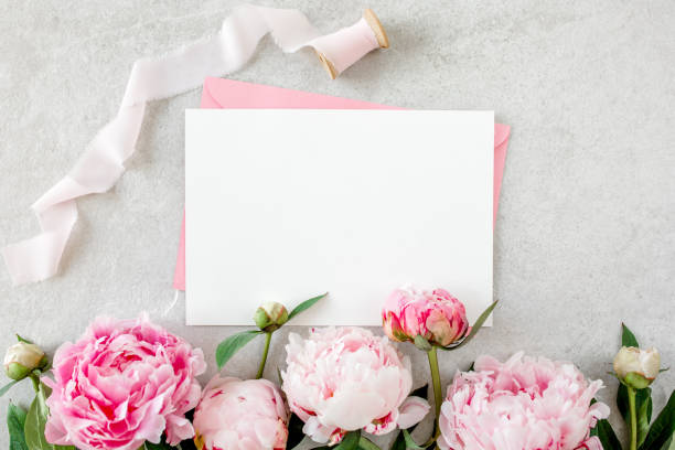 istock Mockup invitation, blank paper greeting card, pink envelope and peonies on gray stone table. Flower background. Flat lay, top view 1271710134