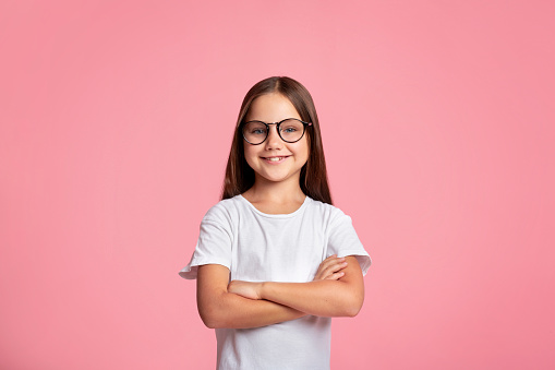 Smart kid. Cheerful little child in glasses with crossed arms, isolated on pink background, copy space
