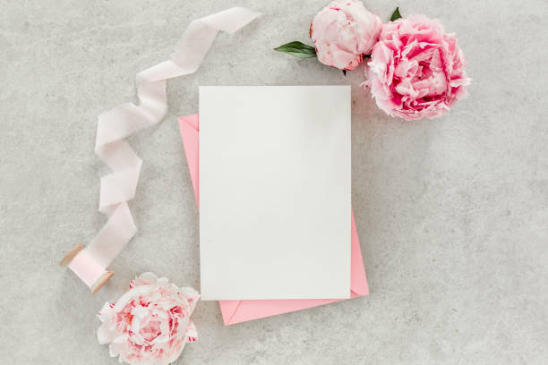 istock Mockup invitation, blank paper greeting card, pink envelope and peonies on gray stone table. Flower background. Flat lay, top view 1271710639