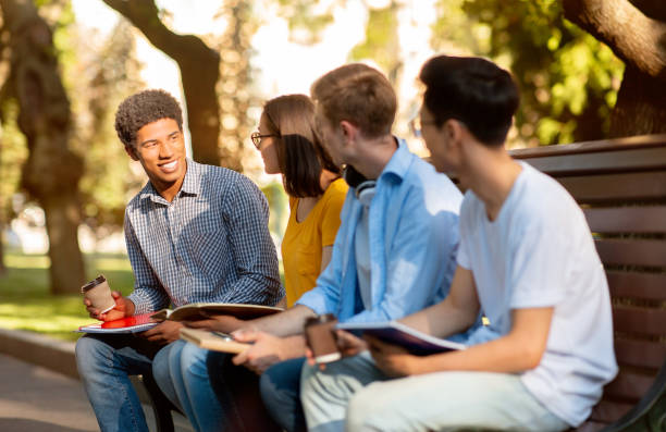 istock Four High-School Students Discussing Classes Sitting On Bench In Park 1271712625