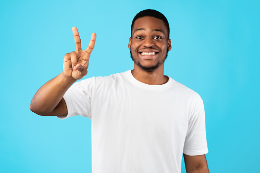 African Man Showing Number Two Posing On Blue Studio Background, Smiling To Camera. You're Second Concept