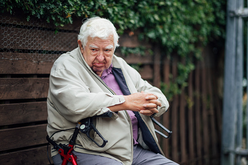 A shot of a senior man sitting on his mobility walker. He is wearing casual clothing and in a community garden.