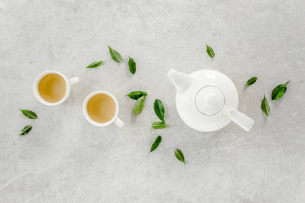 istock Herbal tea with two white tea cups and teapot, with green tea leaves. Flat lay, top view. Tea concept 1271714919