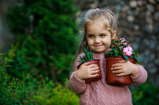 Copy space shot of sweet little girl holding two pots with beautiful flowers that she re-potted while gardening in her back yard. She is smiling and looking away.