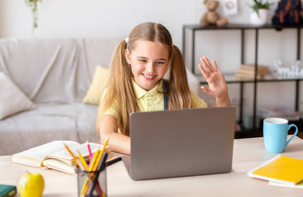 istock Girl sitting at desk, using laptop and waving at camera 1271720590