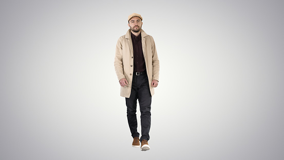 Full length shot. Man with dark beard in light trench coat walks on gradient background. Professional shot in 4K resolution. 006. You can use it e.g. in your commercial video, business, presentation, broadcast