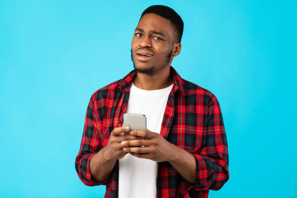 istock Unsure Black Man Holding Cellphone Posing Over Blue Background 1271723668