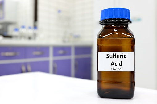 Selective focus of strong sulfuric acid chemical in brown amber glass bottle inside a laboratory with copy space.