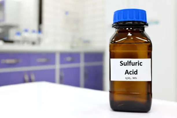 Photo of Selective focus of strong sulfuric acid chemical in brown amber glass bottle inside a laboratory with copy space.