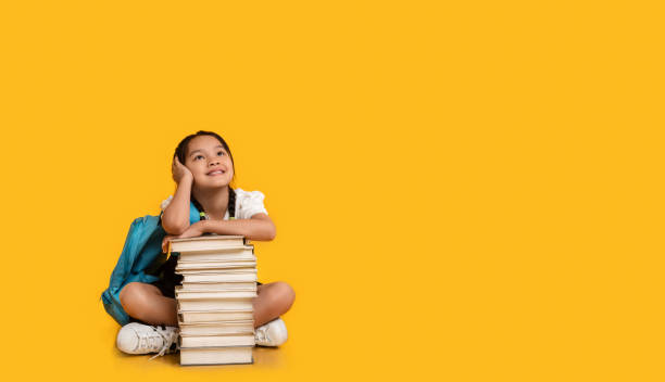 istock Chinese School Girl Sitting At Books Stack On Yellow Background 1271724510