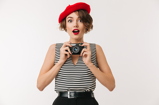Portrait of a joyful woman wearing red beret holding photo camera and looking at camera isolated over white background