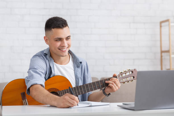 istock Smiling young man watching online lesson, playing guitar and makes notes 1271726581