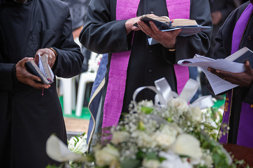 Three Anglican priests attending a funeral, next to the grave