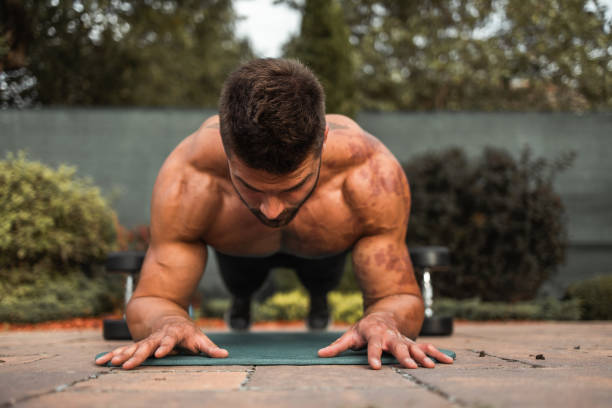Shot of a shirtless muscular young man doing strength exercise on yoga mat in the backyard.