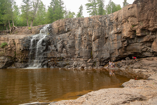 Three young children (two sisters and their younger brother) exploring the cliffs and water near a waterfall at Gooseberry Falls State Park.