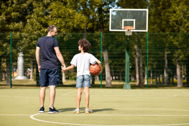 istock Man posing with little boy on basketball pitch back view 1271730918