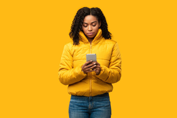 istock Serious African Girl Using Smartphone Wearing Winter Clothes, Studio Shot 1271732895