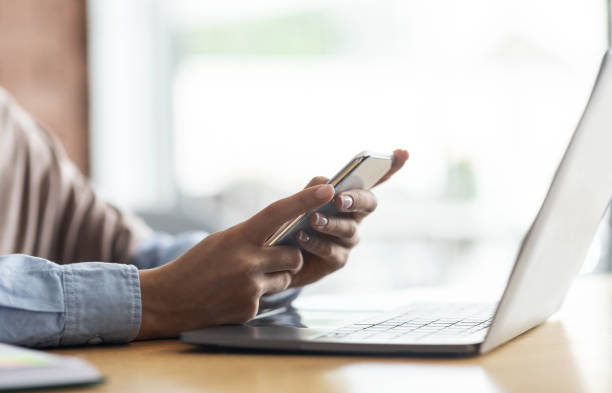istock Female hands holding mobile phone and using laptop 1271737797
