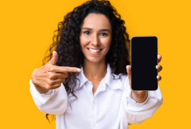 istock Smiling Brunette Woman Pointing On Blank Black Smartphone Screen, Mockup Image 1271737819