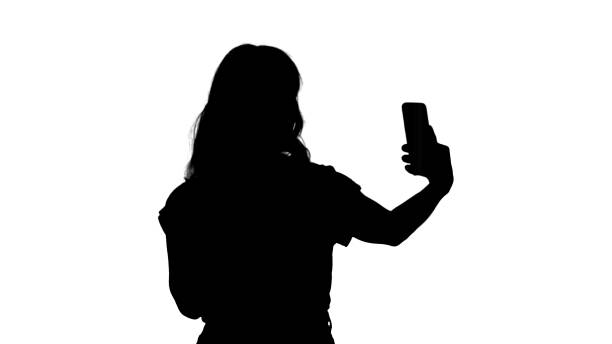istock Silhouette Cheerful female blogger recording video to front camera of modern telephone while walking 1271739479