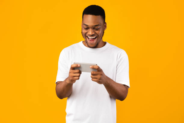 istock Excited Black Man Playing Games On Smartphone, Yellow Background 1271740194