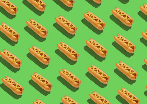 istock Lots of classic hotdogs with mustard sause over green background, creative pattern 1271742131