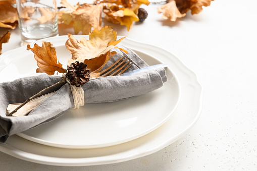 Elegant fall table setting with autumn leaves and white plate on white table. Close up.