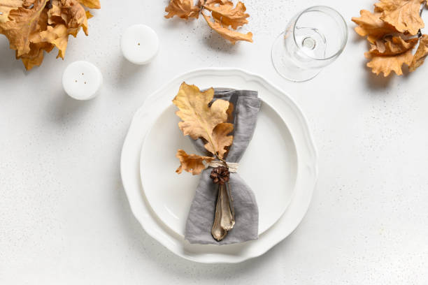 Fall table setting with autumn leaves and white plate on white table. View from above.