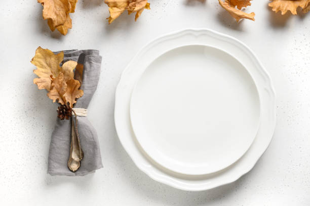 Fall table setting with autumn leaves and white plate on white table. Space for design.