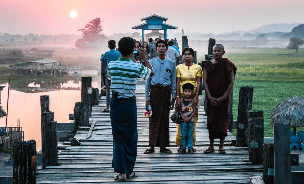 Family posing at the bridge of U bein. Famous wooden bridge in sunset. Myanmar family taking a photo with Monk Amarapura stock pictures, royalty-free photos & images