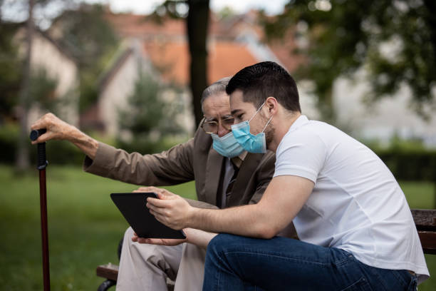 istock Two generations, a grandson and a grandfather, sit on a bench using a tablet and talking under masks 1271747963