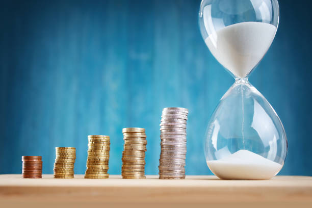 istock Clock with stacked coins and hourglass on blue background 1271747988