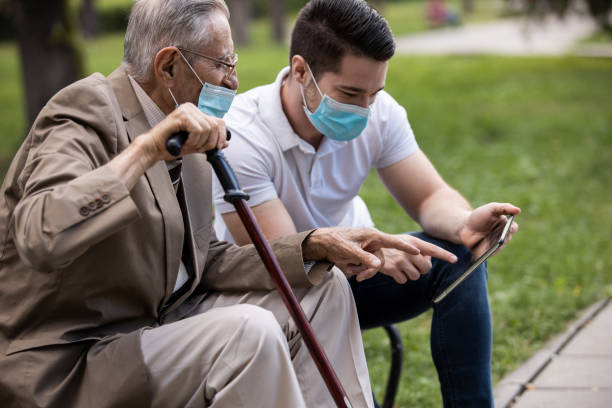 istock Two generations, a grandson and a grandfather, sit on a bench using a tablet and talking under masks 1271748429