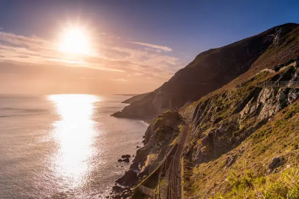 Dramatic sunrise with sun star on a Cliff Walk between Bray and Greystones with beautiful coastline, train tracks, cliffs and Irish Sea, Ireland