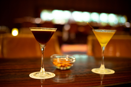 glass with brown alcoholic drink and piece of ice stands on the bar. Blurred view of restaurant in background.