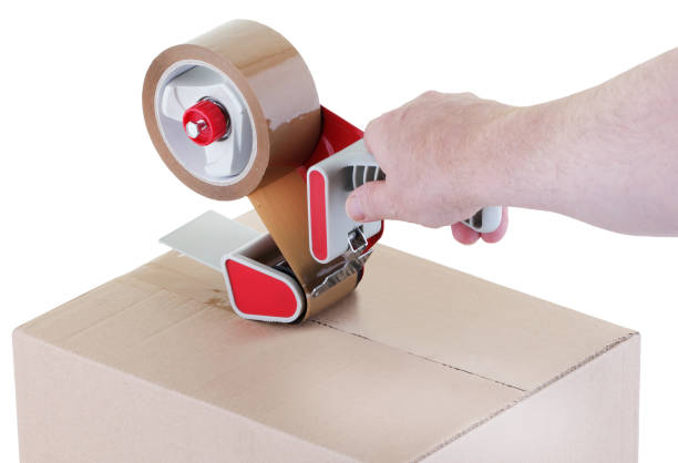 sealing a shipping cardboard box with adhesive tape dispenser sealing a shipping cardboard box with an adhesive tape dispenser nigel pack stock pictures, royalty-free photos & images