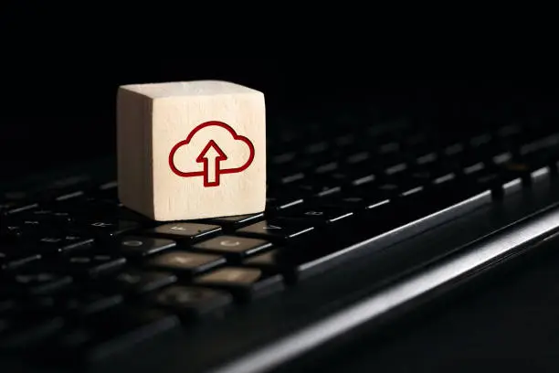 Photo of Cloud computing upload icon on wooden cube with computer keyboard. Remote download technology concept.