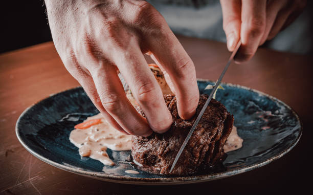 istock chef hand cut Grilled beef steak filet mignon in plate on wooden table 1271755668