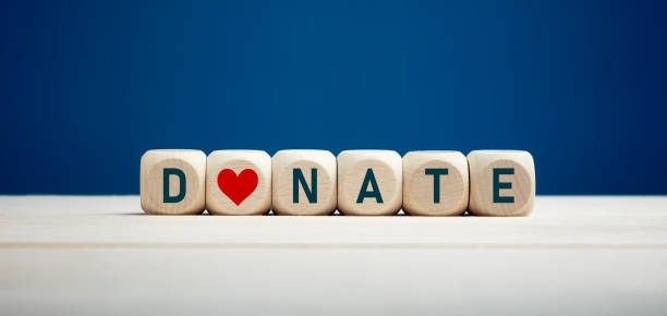 la palabra donar en bloques de madera con icono del corazón contra el fondo azul. caridad y donación. - generosidad fotografías e imágenes de stock