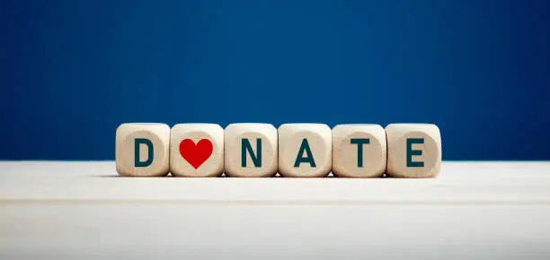 The word donate on wooden blocks with heart icon against blue background. Charity and donation concept.