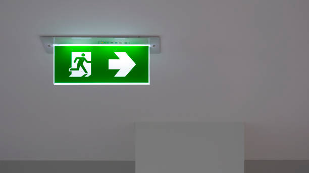 segnale di uscita di emergenza verde sul soffitto all'interno dell'edificio - fire exit sign foto e immagini stock