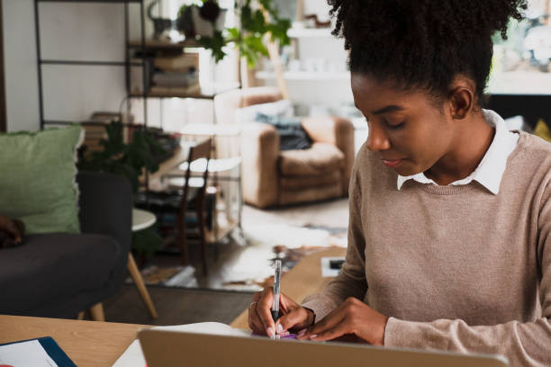 istock Female student studying for online exam using stationary and notepad siting in front on laptop in modern kitchen 1271756360