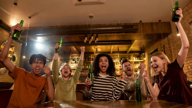 grite. amigos felizes no bar assistindo jogos esportivos na tv juntos, bebendo cerveja e celebrando a vitória. pessoas, lazer, amizade e conceito de entretenimento - time table - fotografias e filmes do acervo