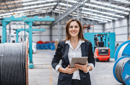 Happy industrial attractive supervisor businesswoman with suit working with tablet pc and look at camera posing in factory building