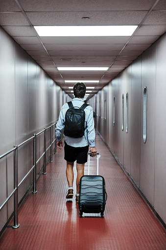 Rearview shot of a young man waking through an airport with his luggage